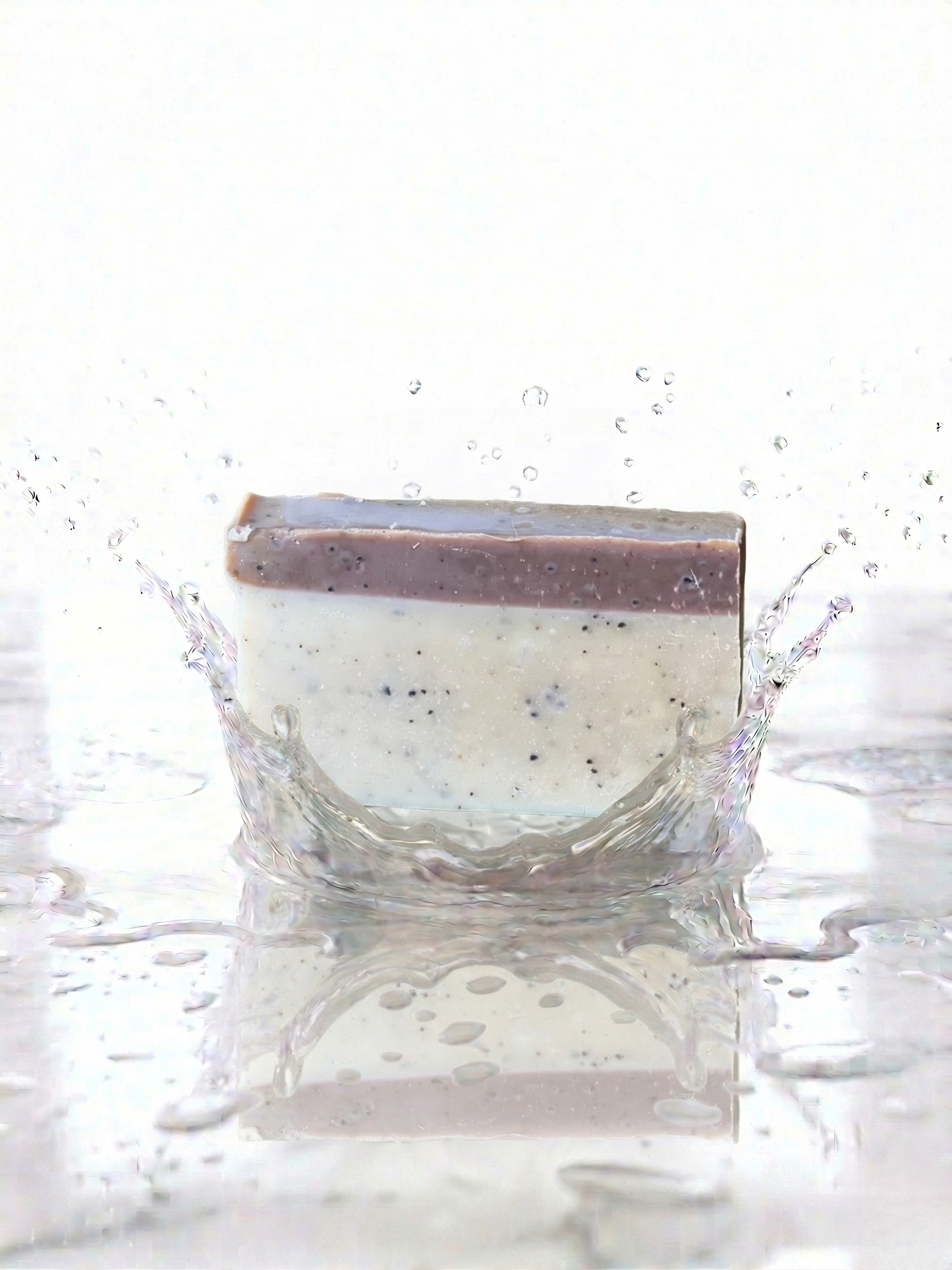 Bar of soap with a brown coffee top and white bottom splashing in water on a white background