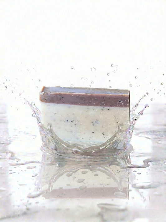 Bar of soap with a brown coffee top and white bottom splashing in water on a white background