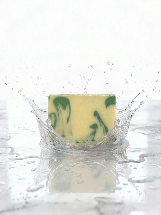 Bar of soap with green swirls splashing into water on a white background