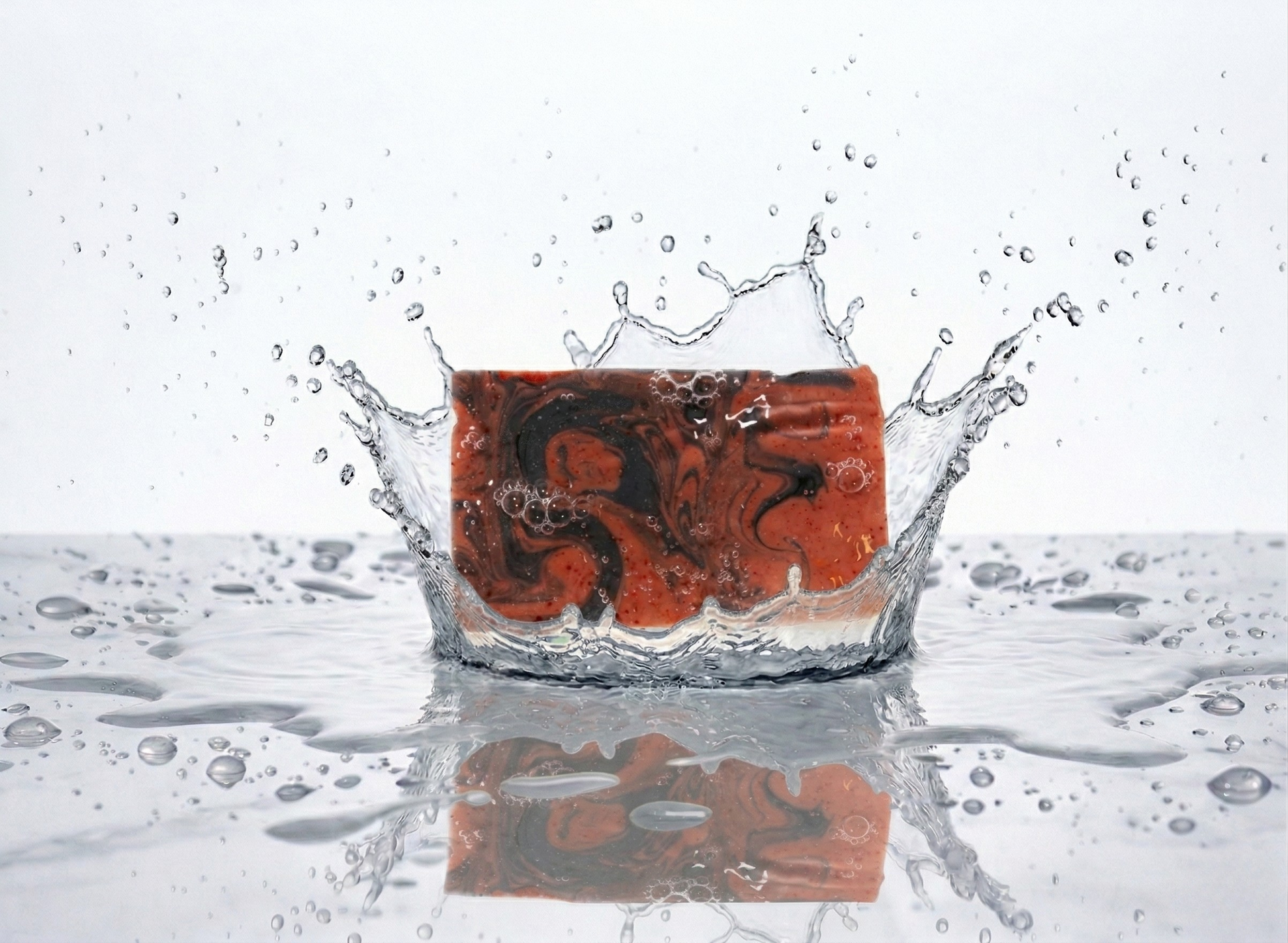 Bar of soap with a red and black marbled pattern splashing into water on a reflective surface.